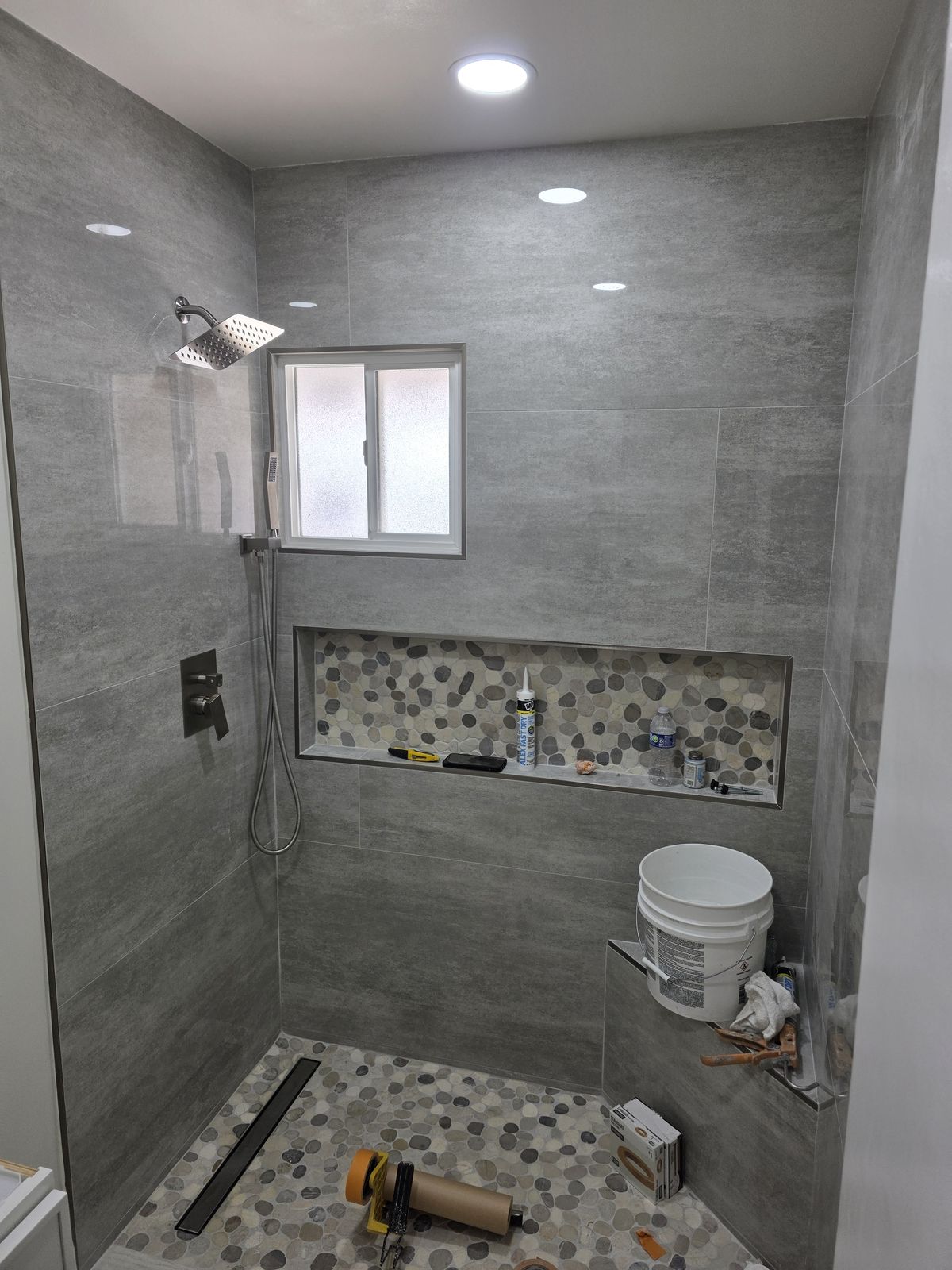 Walk-in shower tile work in progress with pebble floor and linear drain, Buena Park