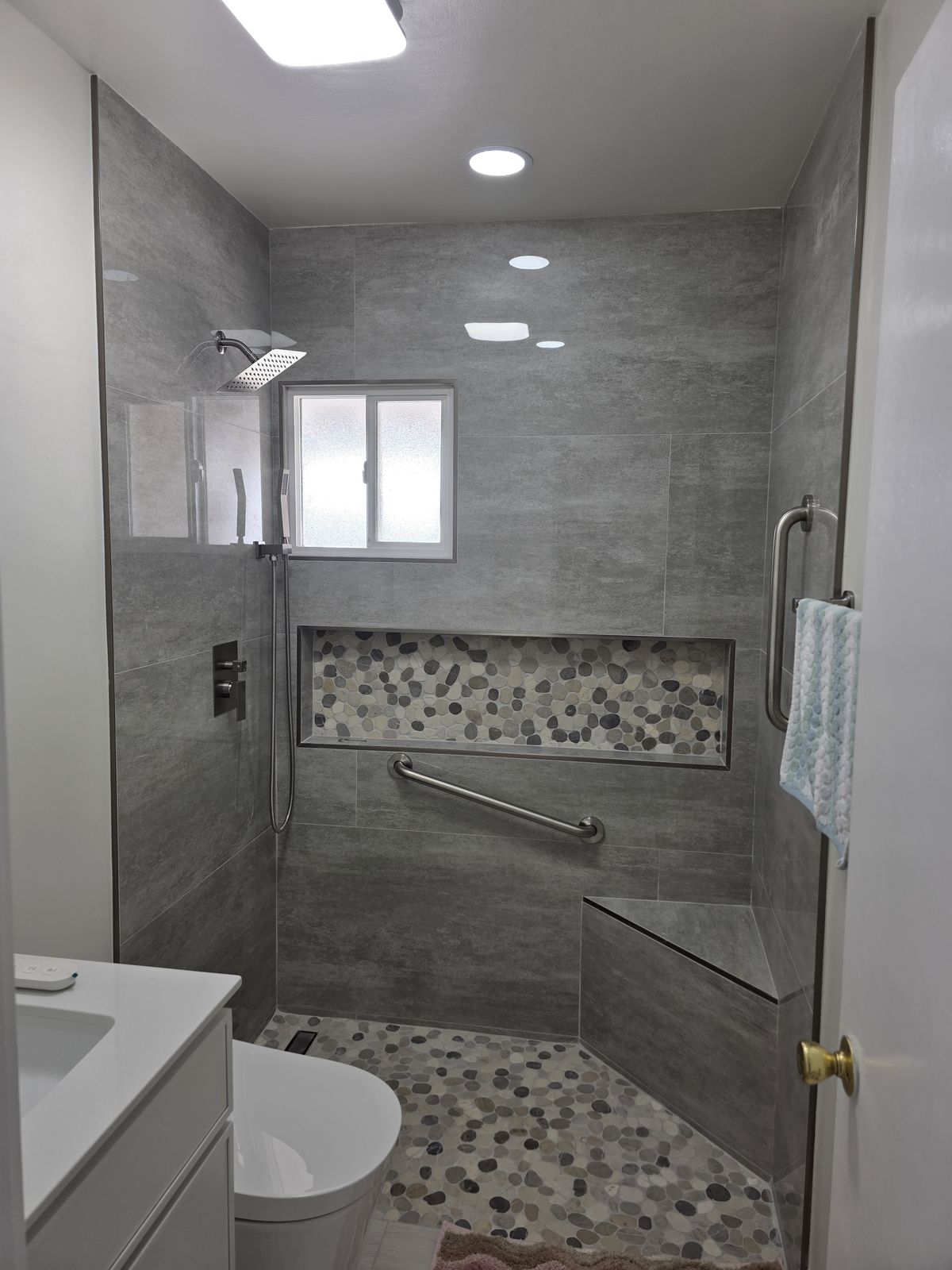 Gray porcelain walk-in shower with pebble niche, bench and grab bar, Buena Park